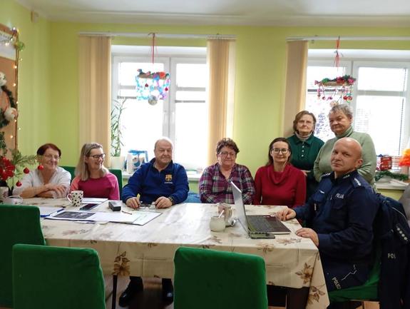 policjant siedzący przy stole z seniorami